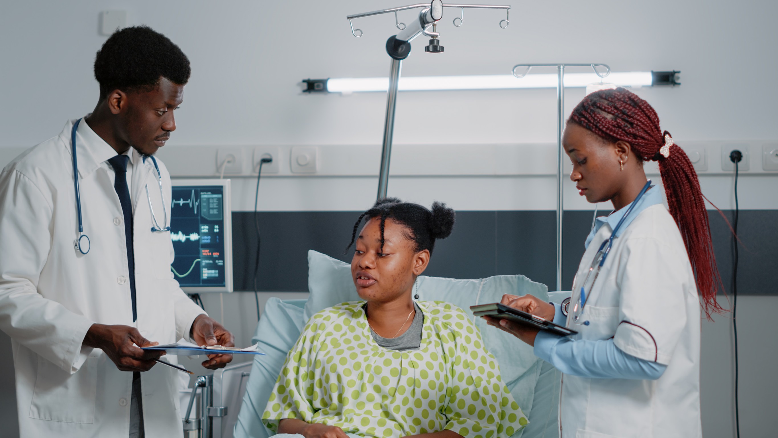 Team Of African American Doctors Consulting Sick Patient In Bed
